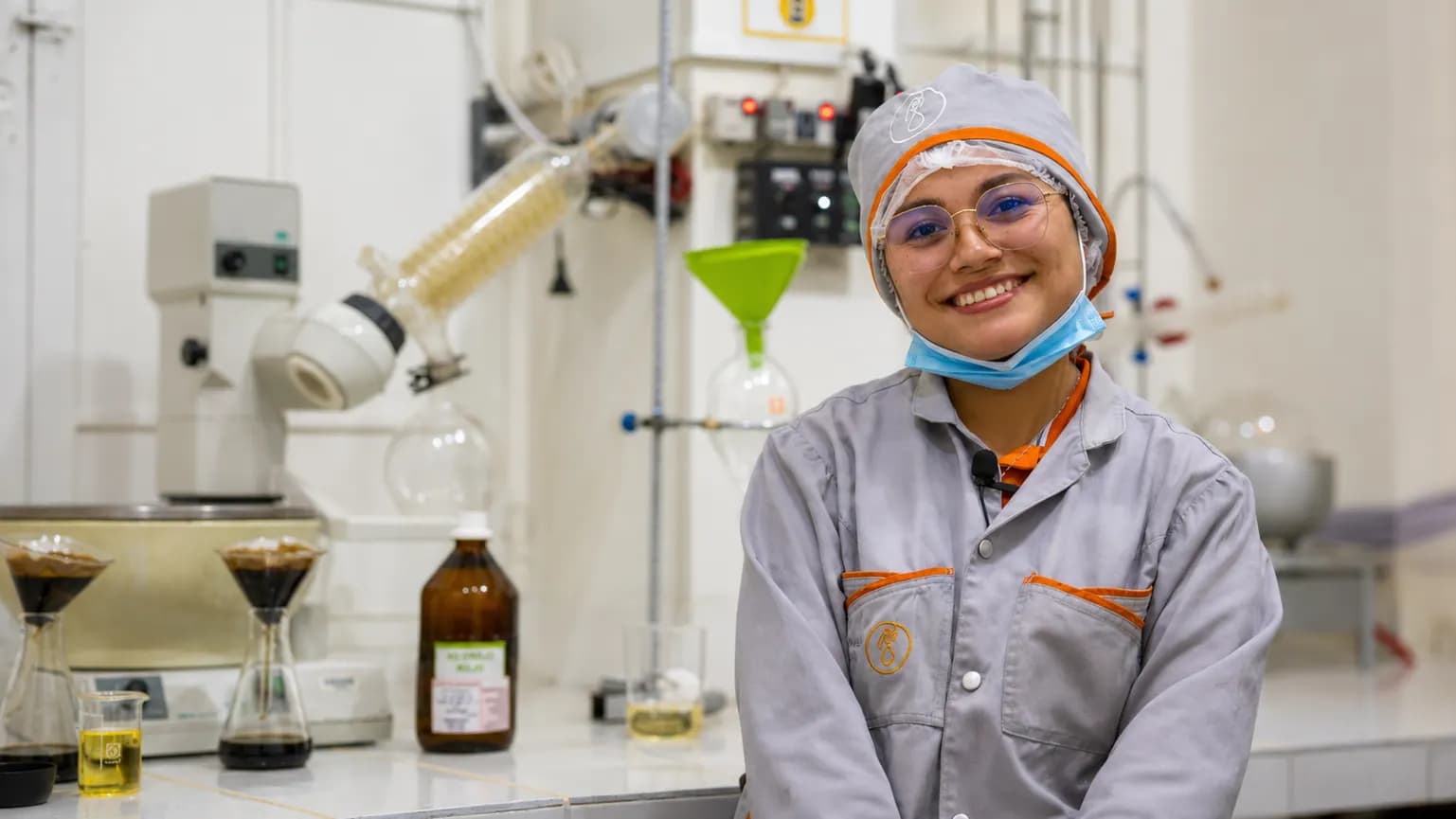 Quimica boliviana sonriendo en el laboratorio de su empresa, rodeada de equipos de destilacion