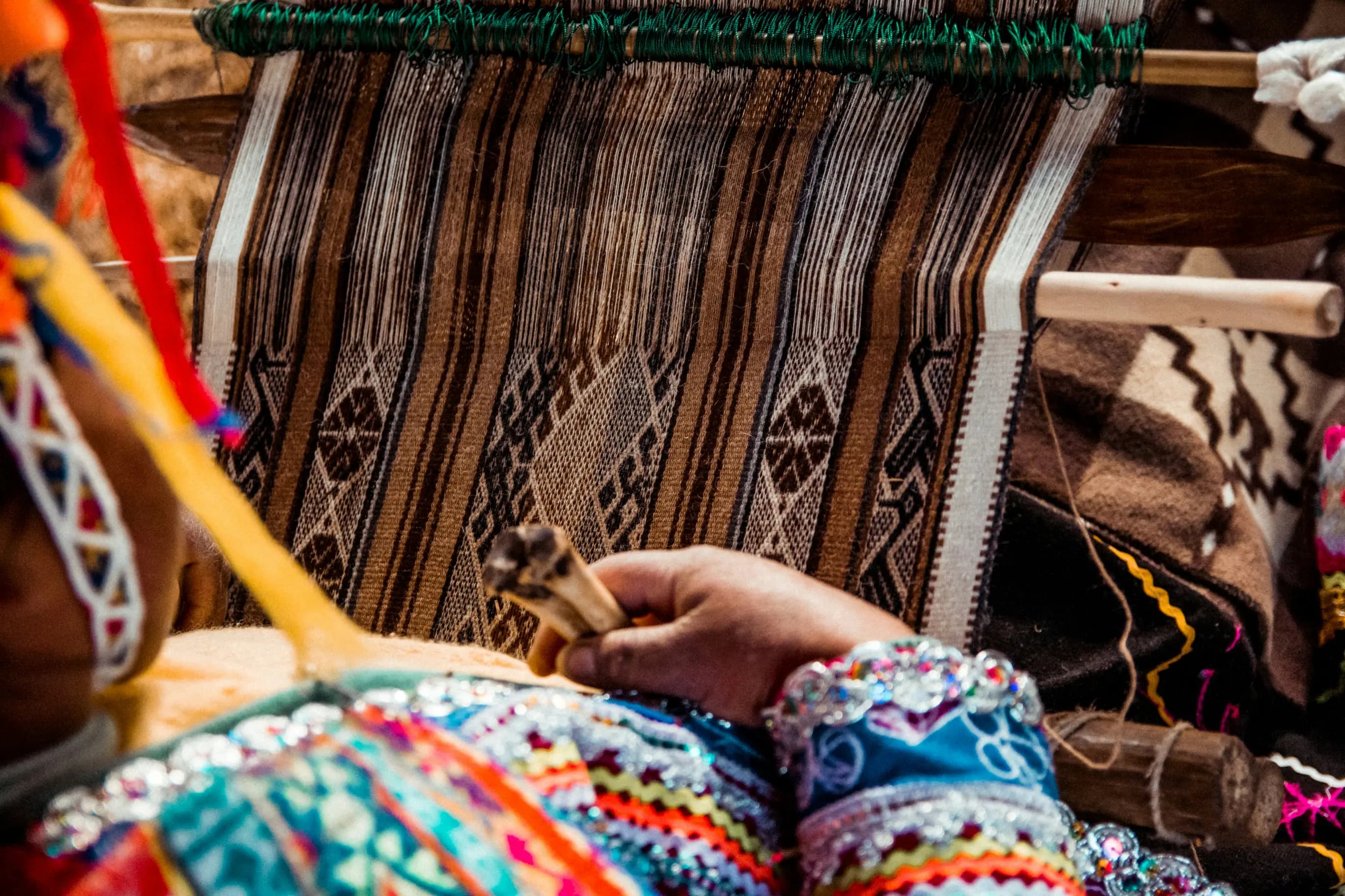 Manos tejiendo en telar tradicional con textiles andinos coloridos